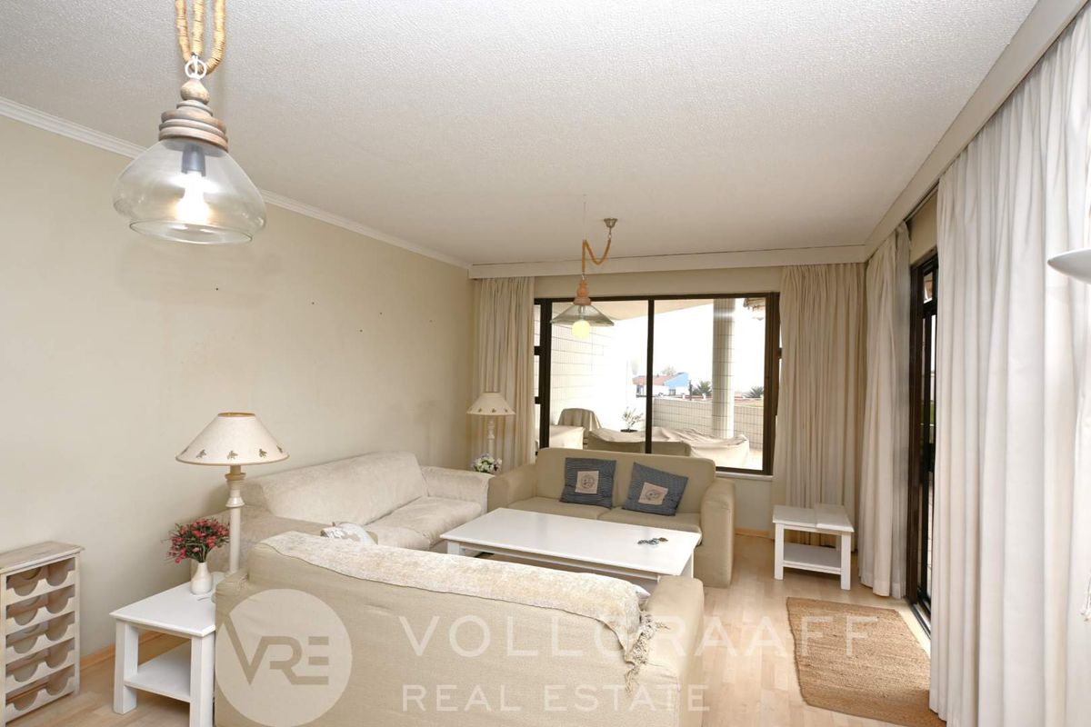 A bright living room featuring laminate flooring and a large sliding glass door that provides access to an outdoor balcony area.