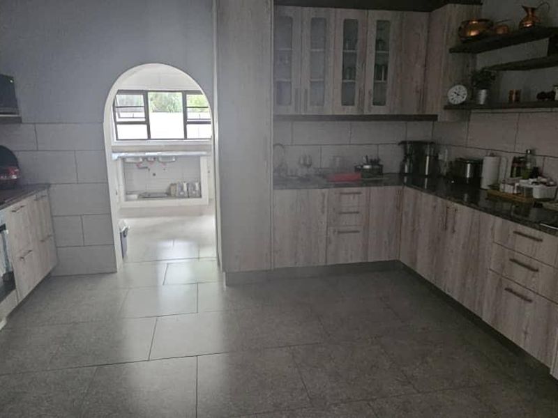 Spacious kitchen featuring light wood-finish cabinetry, stone countertops, built-in oven, and a tiled floor, with an arched doorway leading to a secondary prep area.