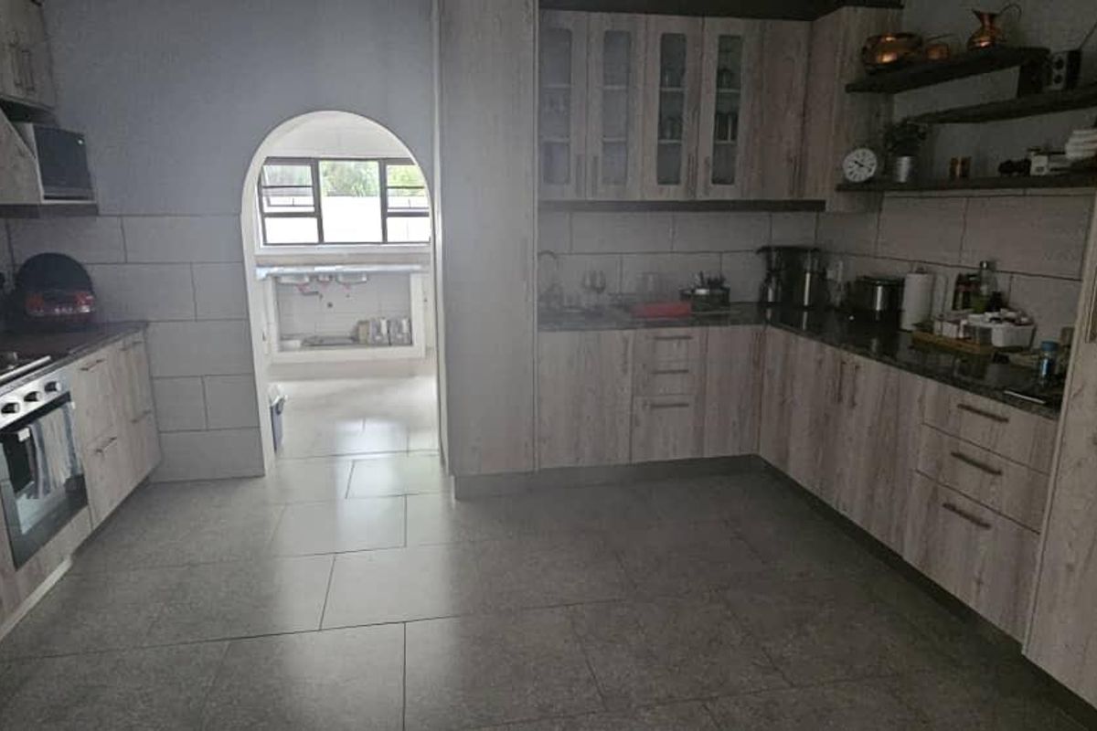 Spacious kitchen featuring light wood-finish cabinetry, stone countertops, built-in oven, and a tiled floor, with an arched doorway leading to a secondary prep area.