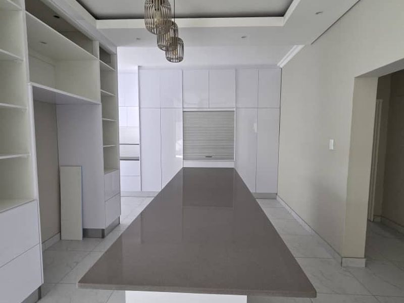 Modern kitchen featuring a large central island with a quartz countertop, sleek white cabinetry, and elegant recessed ceiling lighting with pendant fixtures.