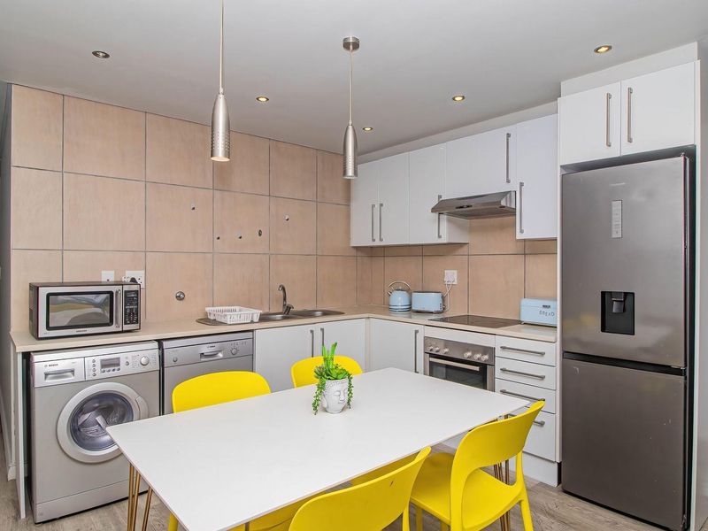 Compact kitchen featuring white cabinetry, tiled splashback, integrated appliances, and recessed lighting, providing a functional and efficient workspace.