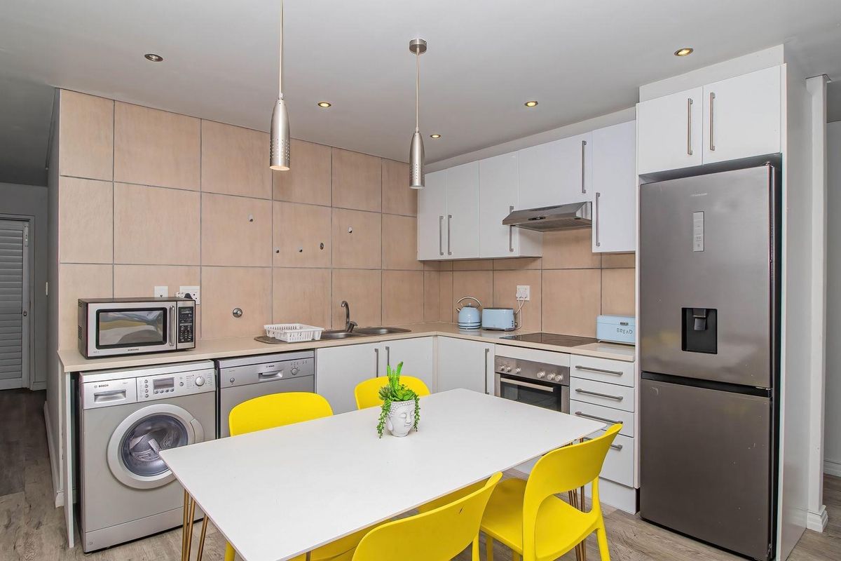 Compact kitchen featuring white cabinetry, tiled splashback, integrated appliances, and recessed lighting, providing a functional and efficient workspace.