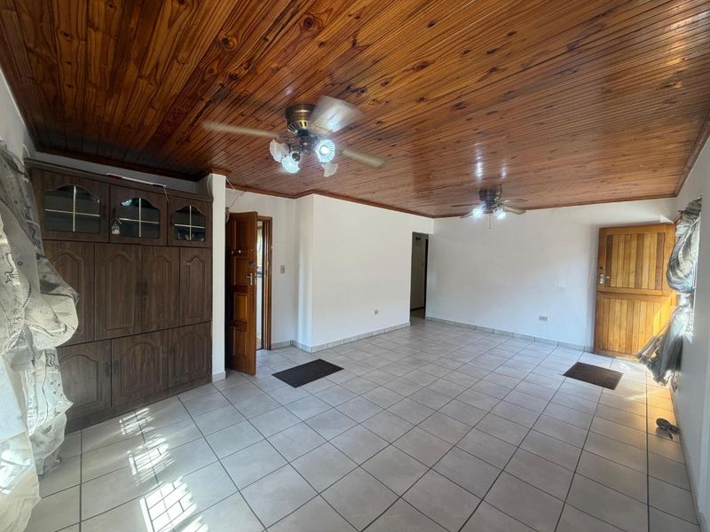 Spacious living area featuring a warm timber tongue and groove ceiling, neutral ceramic floor tiles, and built-in wooden cabinetry.