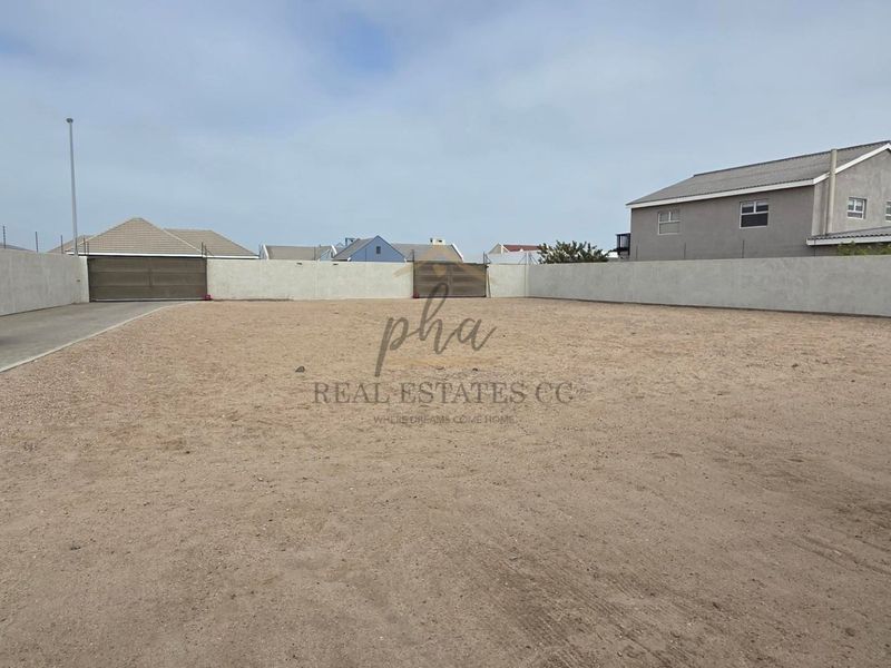 A vacant, level plot of land enclosed by perimeter boundary walls, featuring a paved driveway and gated access.