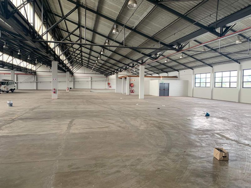 Spacious industrial warehouse featuring high ceilings with exposed steel trusses, polished concrete flooring, and integrated fire safety systems.