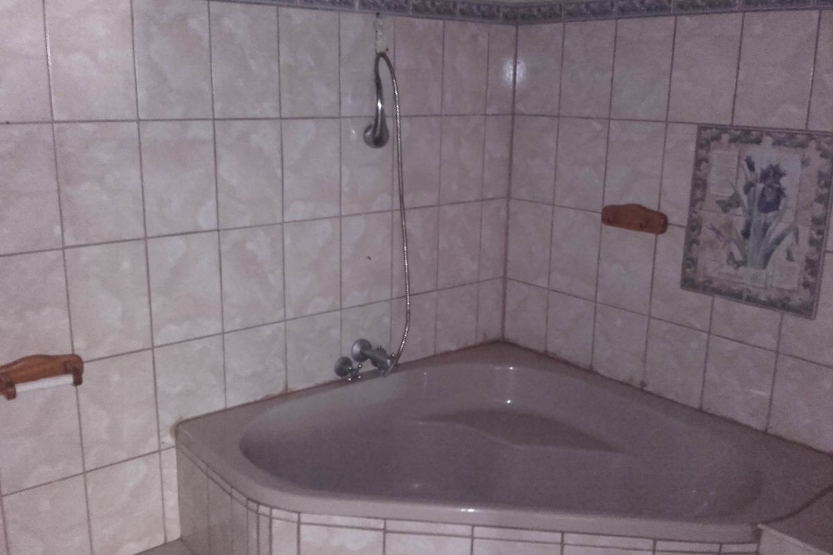 A corner bathtub featuring tiled surround and wall-mounted shower fixture in a dated bathroom setting.