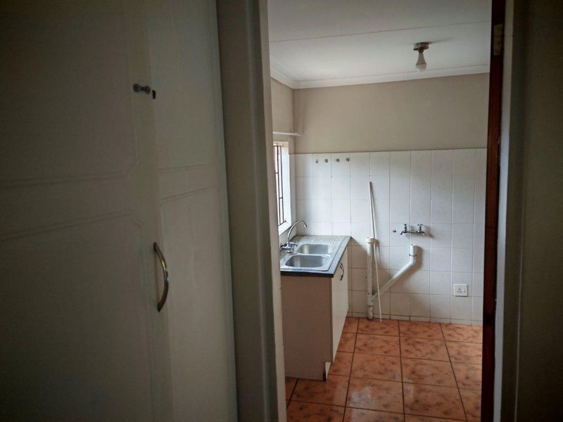 A functional laundry area featuring tiled flooring, a stainless steel sink, and exposed plumbing connections for a washing machine.