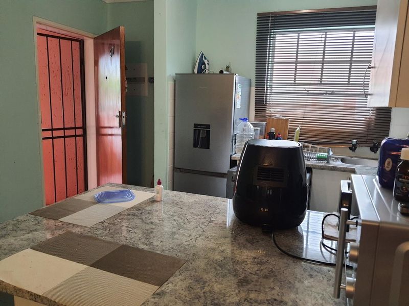 A functional kitchen featuring granite countertops, a sink, and a security gate, offering a practical layout with potential for modern cosmetic updates.