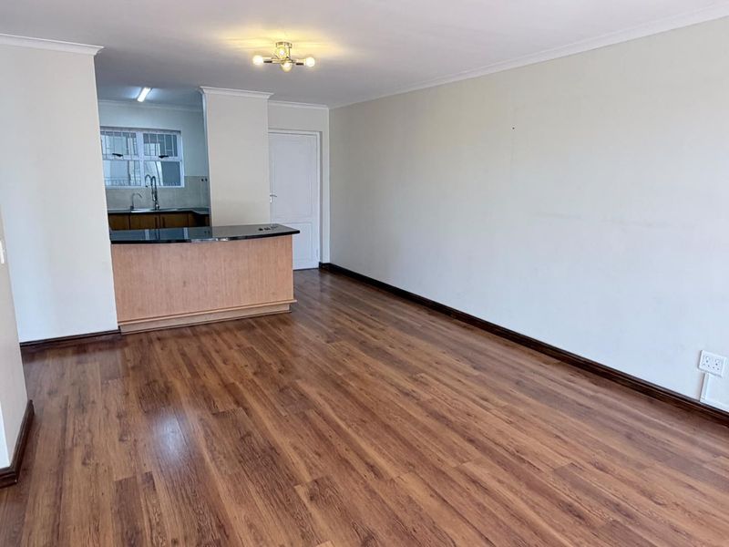 An open-plan living area featuring laminate flooring, a breakfast bar, and a view into the adjacent kitchen space.