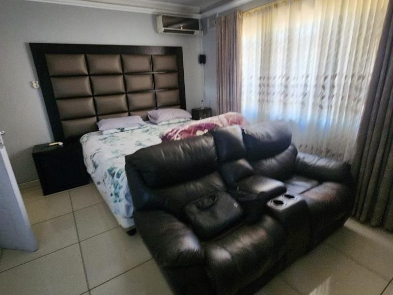 A spacious bedroom featuring tiled flooring, cove cornicing, and a wall-mounted air conditioning unit.