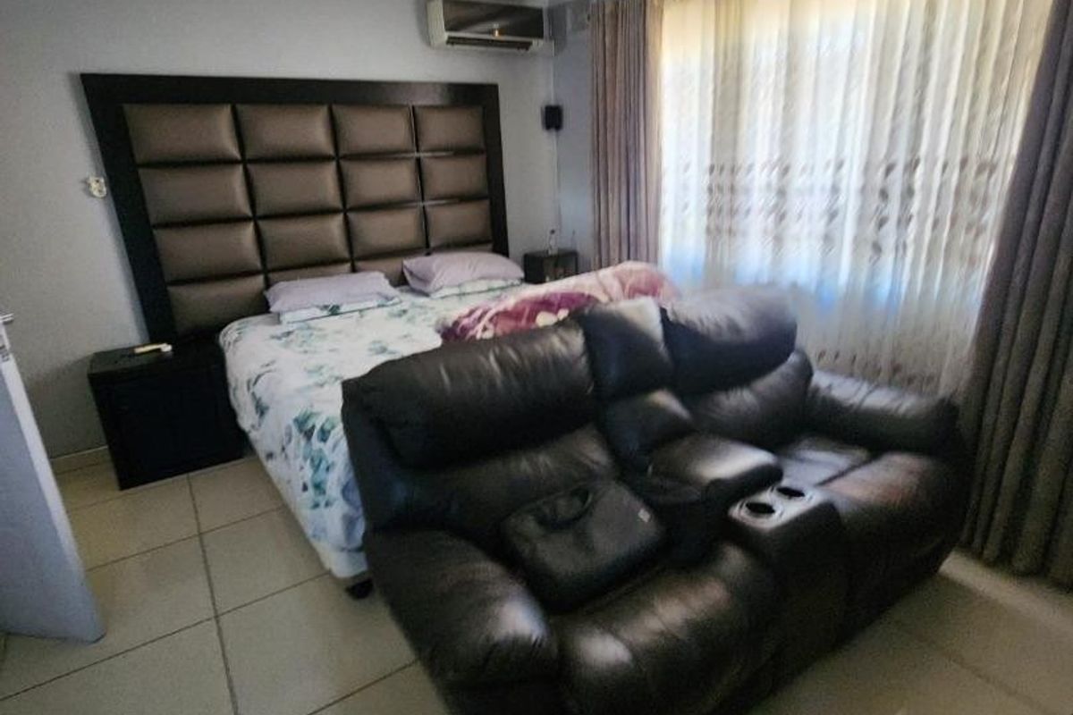 A spacious bedroom featuring tiled flooring, cove cornicing, and a wall-mounted air conditioning unit.