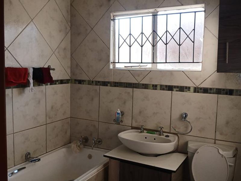 A functional bathroom featuring a built-in bathtub, vanity cabinet with basin, and toilet, finished with tiled walls and security bars on the window.