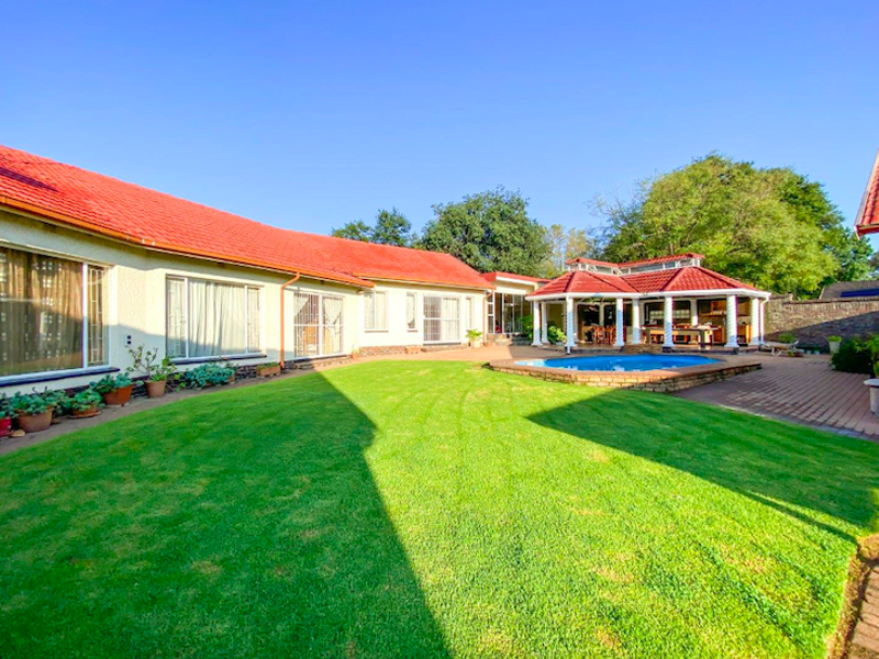 Spacious rear garden featuring a well-maintained lawn, a swimming pool, and a covered outdoor entertainment area with a tiled roof.