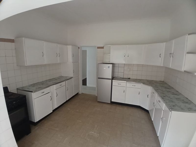A functional kitchen featuring white built-in cabinetry, laminate countertops, and a tiled backsplash, offering a blank canvas for potential modern updates.