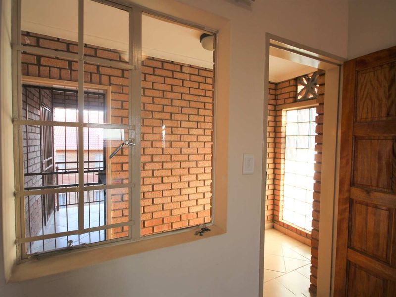 A bright hallway featuring exposed brickwork, a glass block window, and a solid wooden door, providing a unique architectural aesthetic.