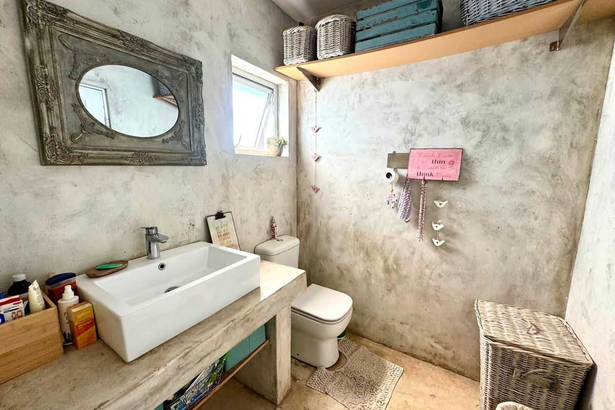 A compact bathroom featuring a concrete vanity with a vessel sink, a standard toilet, and a wall-mounted shelf for storage.