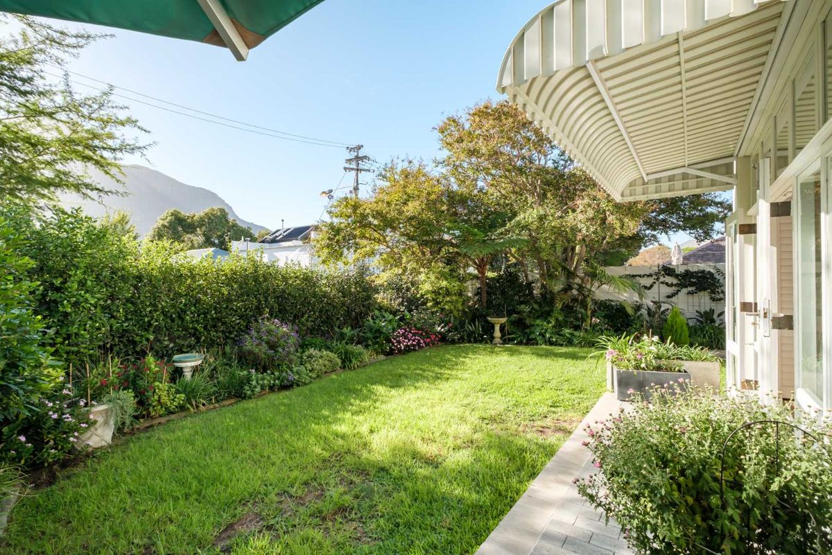 A well-maintained rear garden featuring a paved patio area, established lawn, and mature perimeter hedging, providing a private outdoor space.