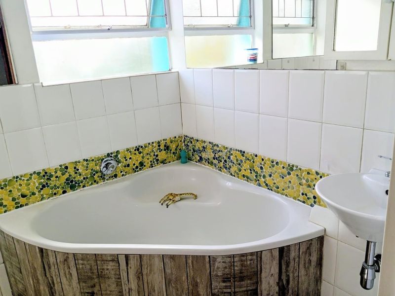 A bathroom featuring a corner bathtub with decorative mosaic tile accents, a wall-mounted basin, and large windows providing natural light.
