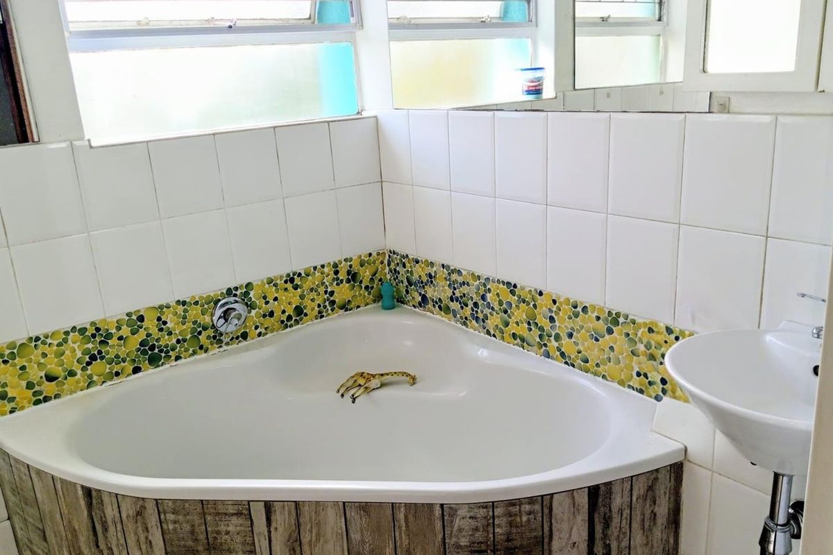A bathroom featuring a corner bathtub with decorative mosaic tile accents, a wall-mounted basin, and large windows providing natural light.
