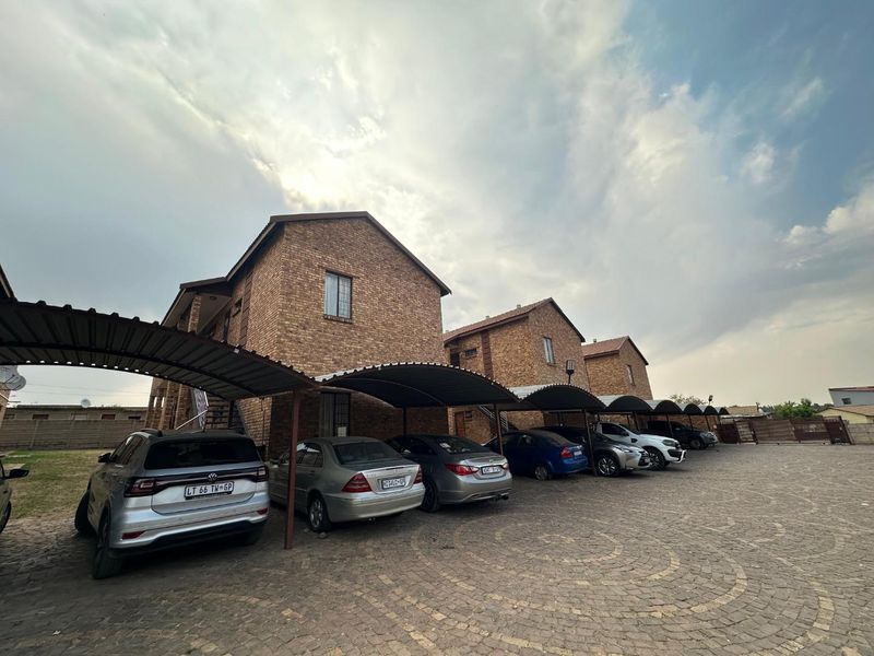 Exterior view of a multi-unit apartment complex featuring face brick facades, covered parking bays, and a paved driveway area.