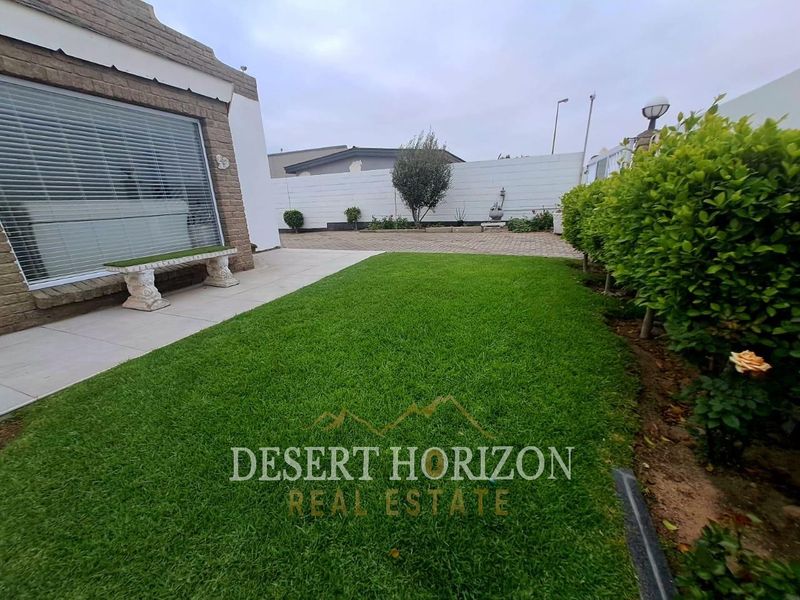 A well-maintained rear garden featuring a neat lawn, paved patio area, and secure boundary walls, providing a private outdoor space.