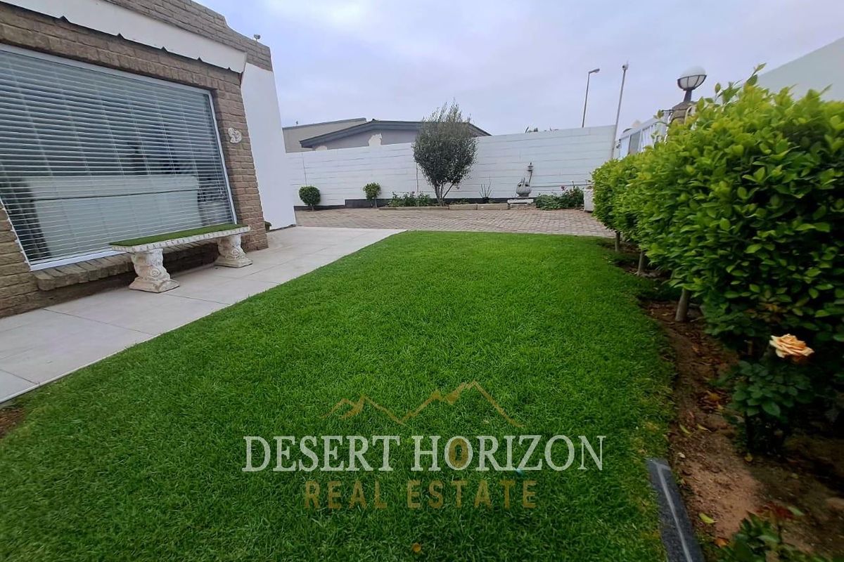 A well-maintained rear garden featuring a neat lawn, paved patio area, and secure boundary walls, providing a private outdoor space.