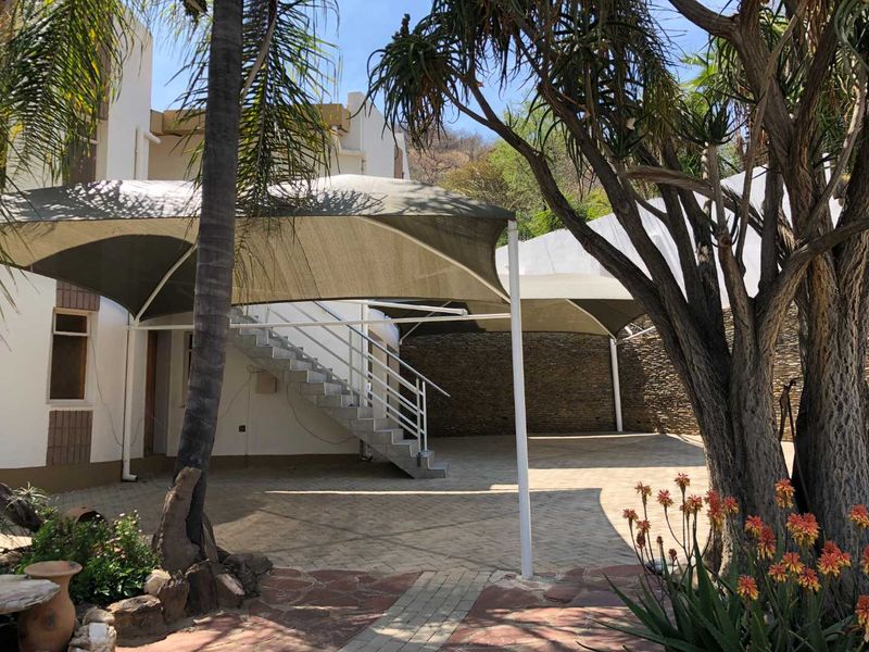 Rear exterior area featuring a paved driveway, shade sail structure, and an external staircase leading to the upper level.
