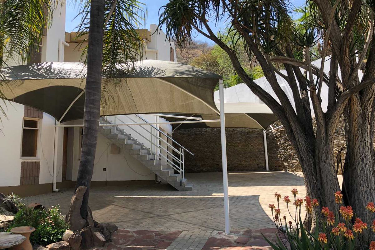 Rear exterior area featuring a paved driveway, shade sail structure, and an external staircase leading to the upper level.
