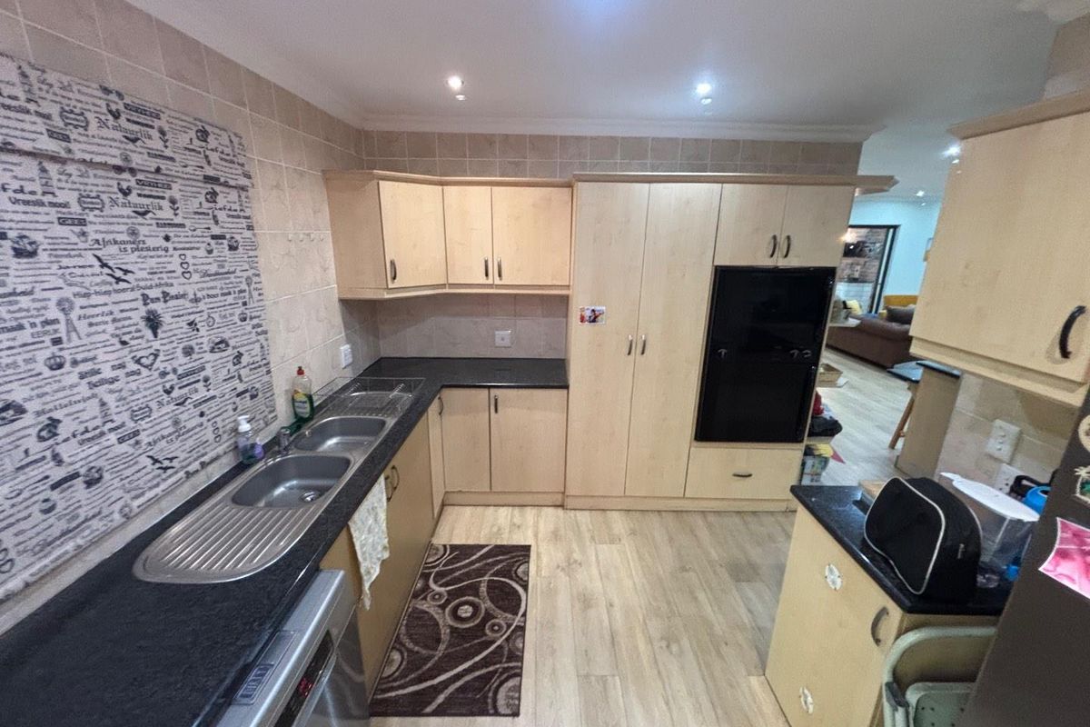 A functional kitchen featuring light wood-finish cabinetry, dark granite countertops, a double stainless steel sink, and integrated oven unit.