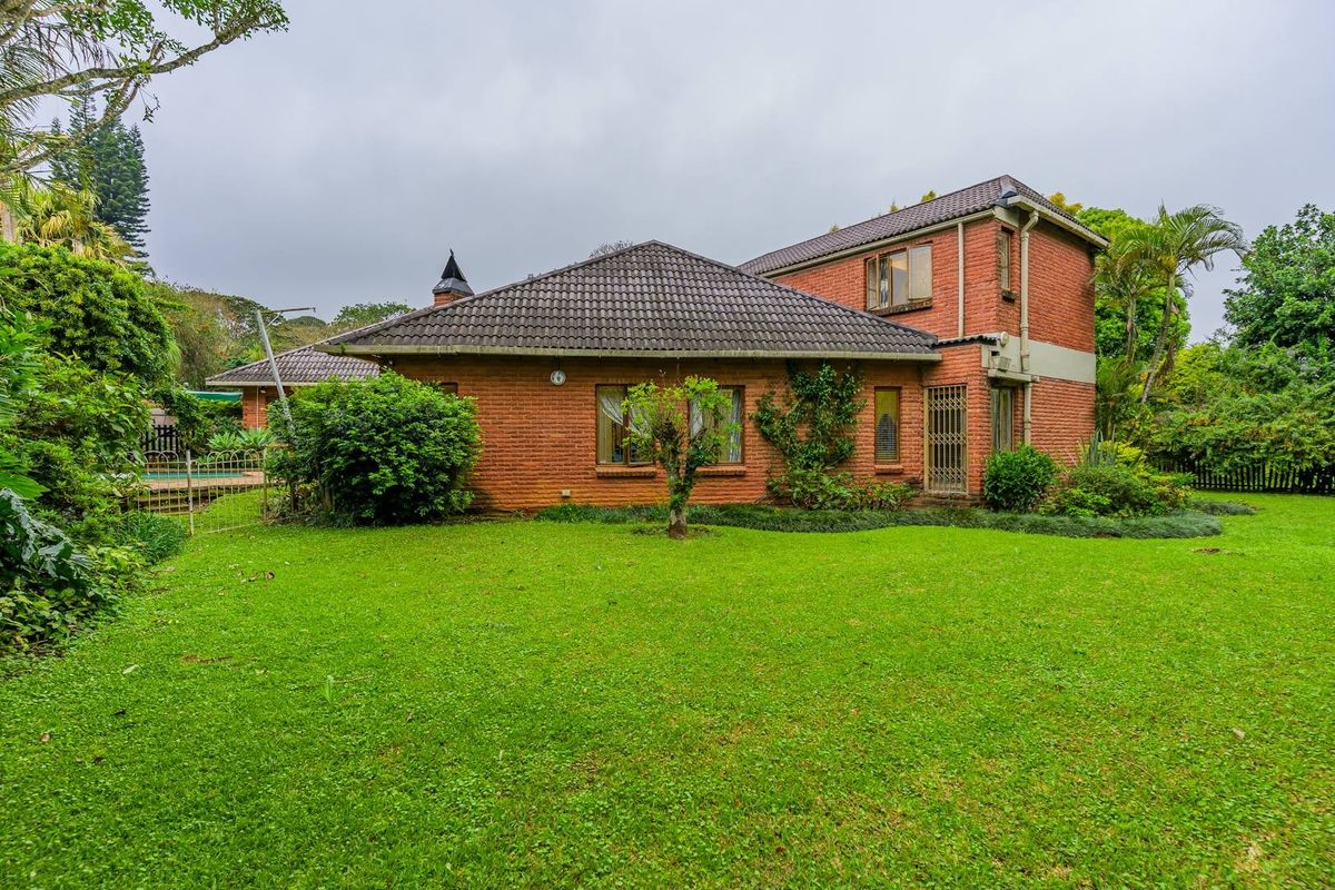 Rear view of a double-story brick house featuring a tiled roof, chimney, and a spacious, well-maintained lawn and garden area.