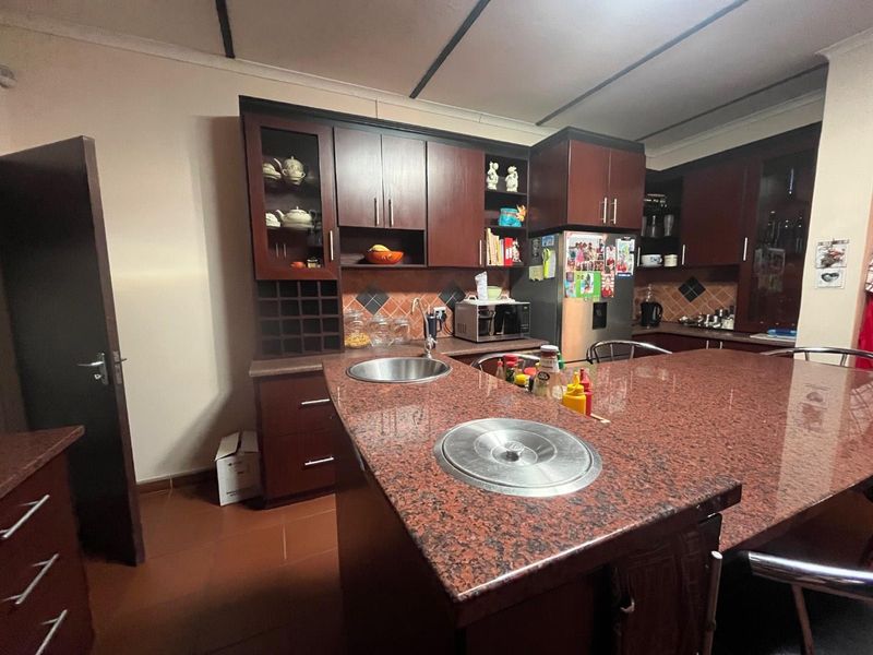 A functional kitchen featuring dark wood cabinetry, granite countertops, a central island with a prep sink, and tiled flooring.