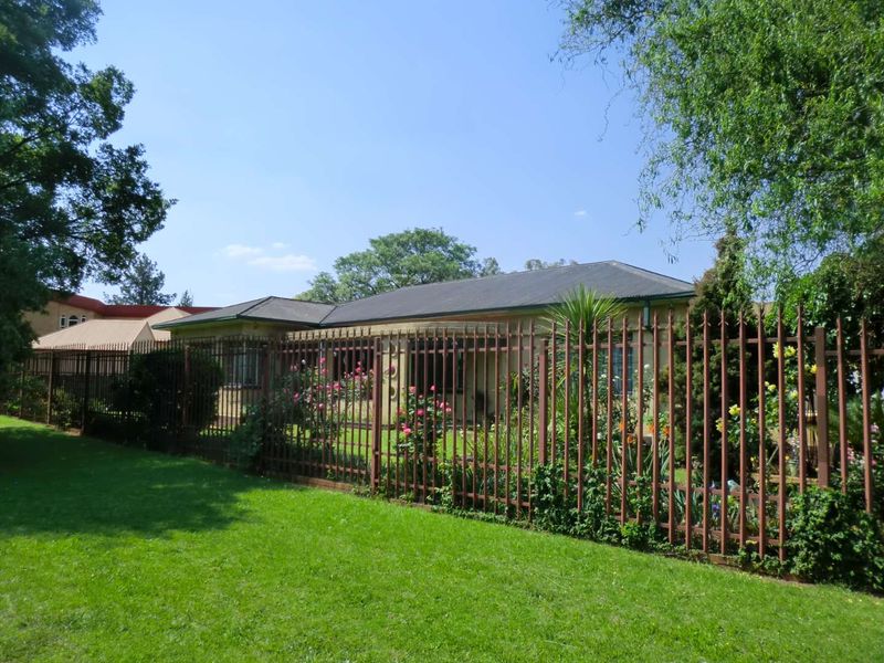 A view of the front exterior of the house, featuring a well-maintained lawn, landscaped garden, and secure metal perimeter fencing.