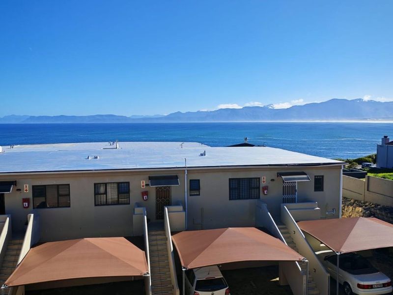 Rear view of the apartment complex featuring carports, external staircases, and a prominent ocean and mountain backdrop.