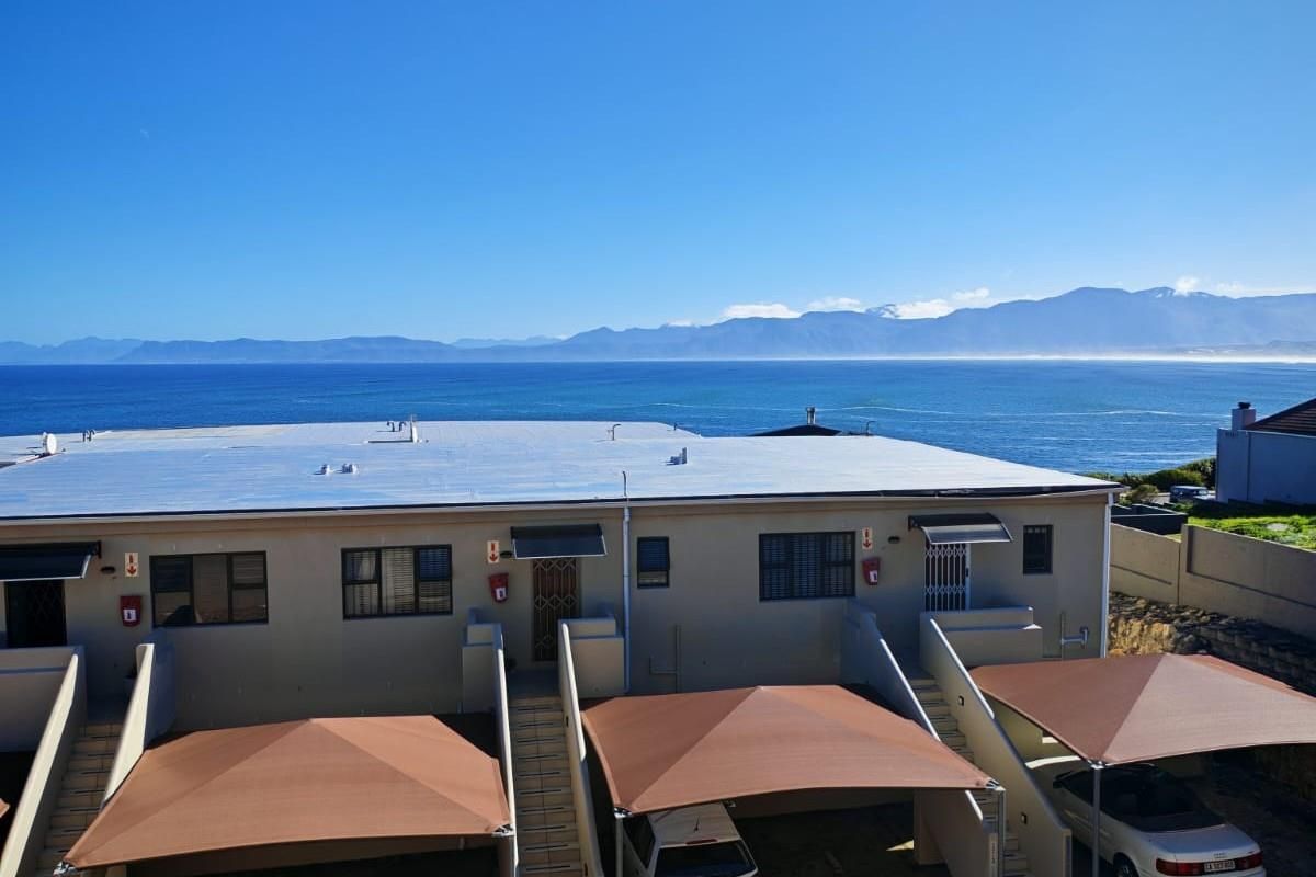 Rear view of the apartment complex featuring carports, external staircases, and a prominent ocean and mountain backdrop.