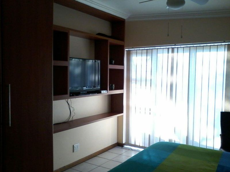 Bedroom featuring built-in wooden shelving, tiled flooring, a ceiling fan, and vertical blinds allowing natural light.