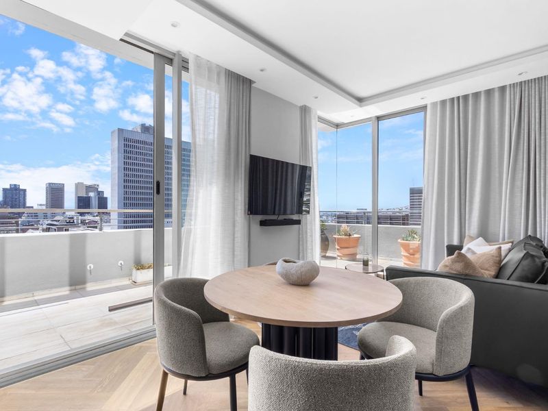 Modern open-plan living area featuring herringbone timber flooring, floor-to-ceiling glass doors, and seamless access to a private balcony with expansive city views.