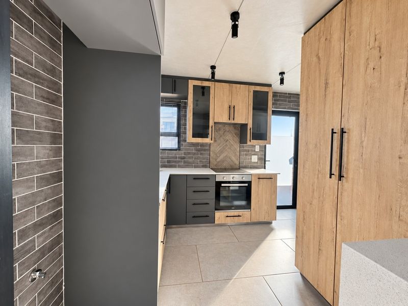 Modern kitchen featuring wood-grain and charcoal cabinetry, stone countertops, built-in oven and hob, tiled backsplash, and large format floor tiles.
