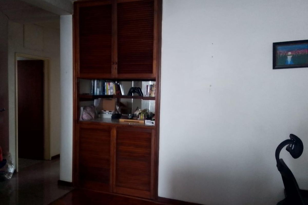 A living area featuring a built-in wooden storage unit with integrated shelving and cabinetry, set against a plain wall with hardwood flooring.