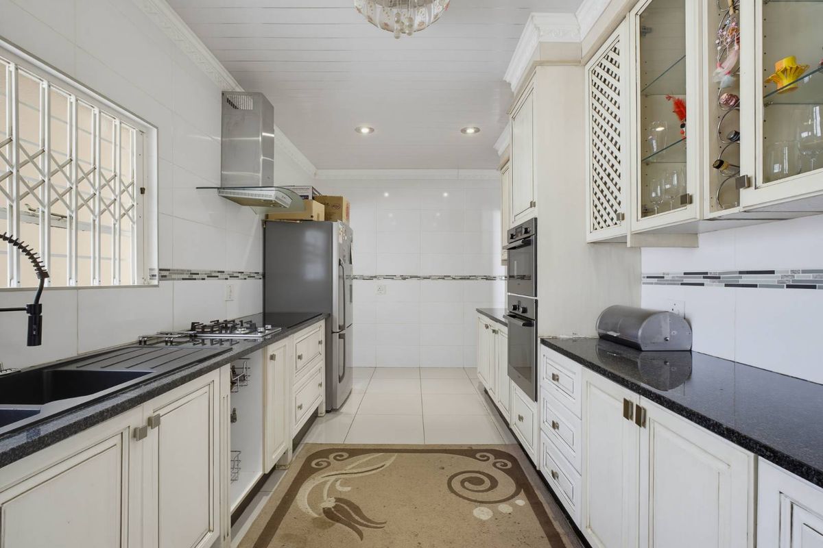 A well-maintained kitchen featuring granite countertops, built-in oven, gas hob, stainless steel extractor fan, and ample cabinetry with tiled finishes.