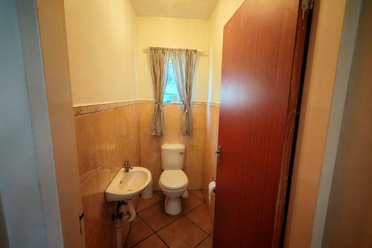 A compact guest bathroom featuring a wall-mounted basin, a standard toilet, and neutral ceramic wall and floor tiling.