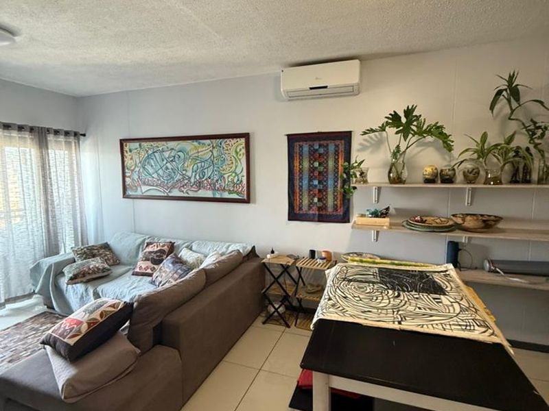 Open plan living area featuring tiled flooring, wall-mounted shelving, and an integrated air conditioning unit with access to a balcony.