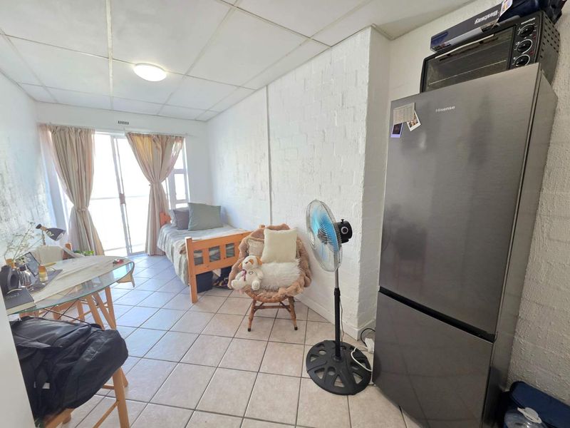 Compact open-plan studio apartment featuring tiled flooring, a painted brick wall, and a sliding glass door leading to an outdoor area.