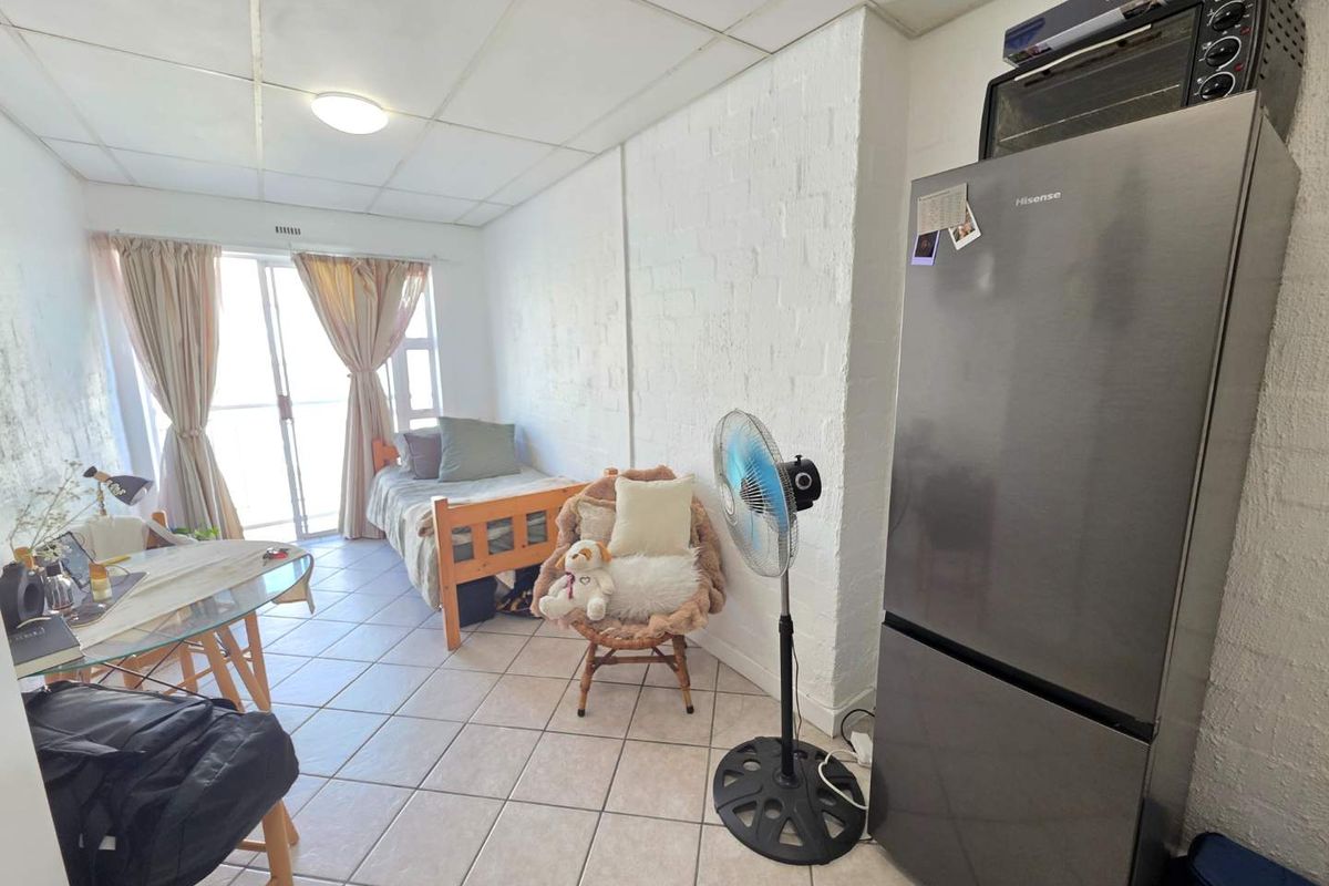 Compact open-plan studio apartment featuring tiled flooring, a painted brick wall, and a sliding glass door leading to an outdoor area.