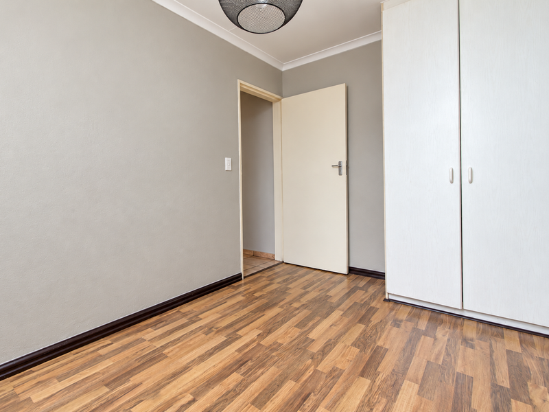 A clean, empty bedroom featuring neutral grey walls, wood-look laminate flooring, and built-in white cupboards, offering a versatile space ready for personalization.