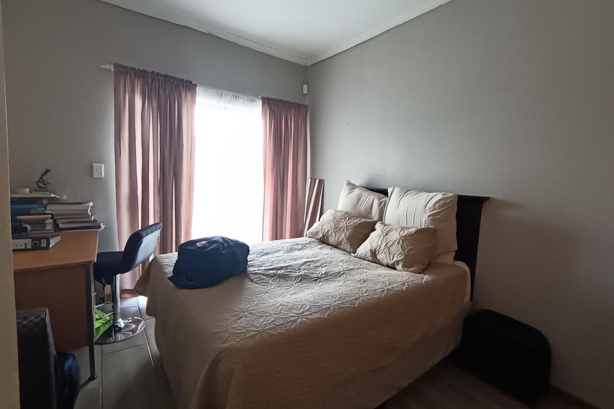 A functional bedroom featuring tiled flooring, neutral wall finishes, and a window with curtain treatments.