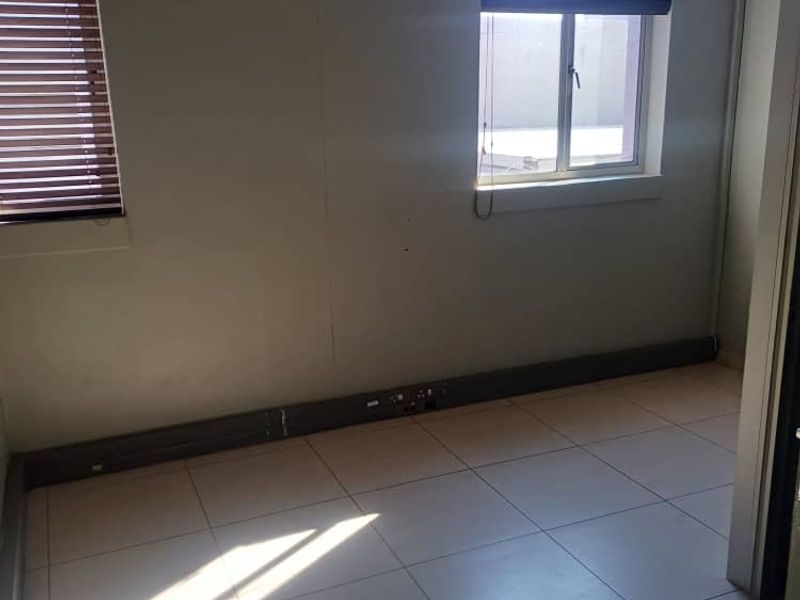 A vacant office space featuring tiled flooring, recessed ceiling lighting, and venetian blinds, providing a clean and functional work environment.