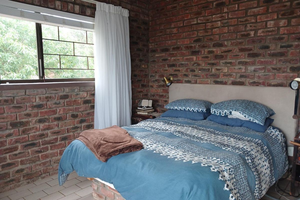 A bedroom featuring exposed face-brick walls, tiled flooring, and a window with security bars, offering a rustic aesthetic.