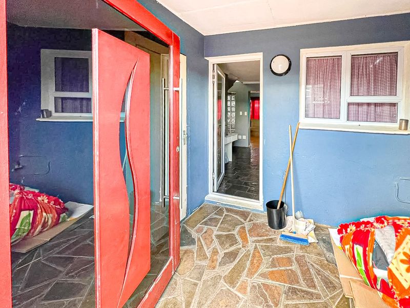 A covered patio area featuring stone flooring, blue painted walls, and access to the interior through a glass panel door.