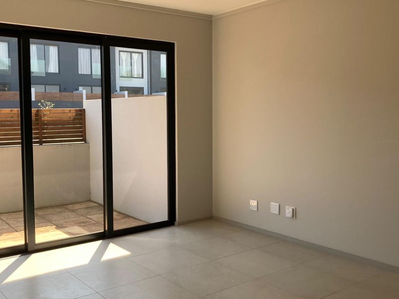 A bright, empty living room featuring neutral tiled flooring and a large sliding glass door providing access to a private patio area.