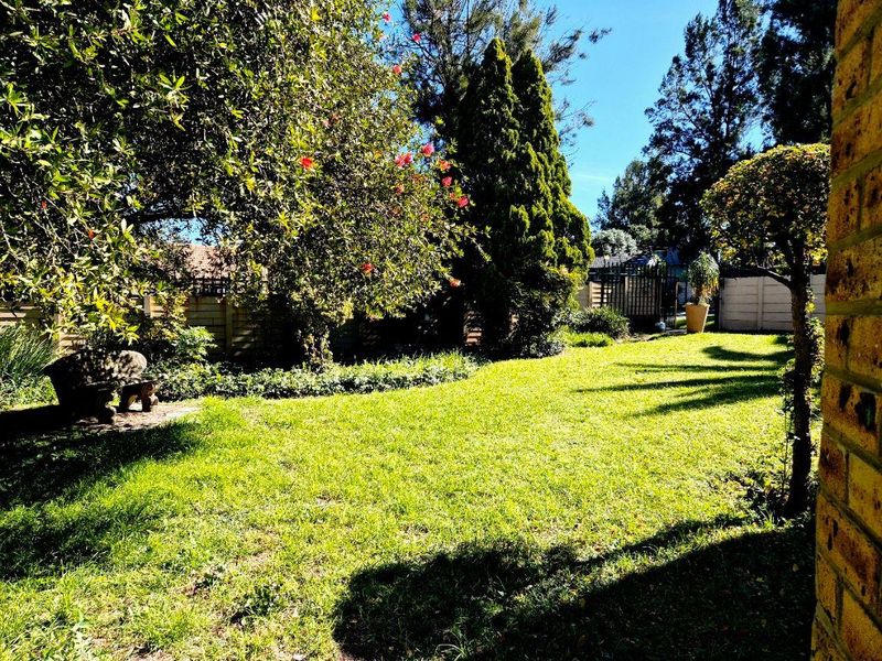 A well-maintained private garden featuring a lush green lawn, mature trees, and secure precast concrete boundary walls.